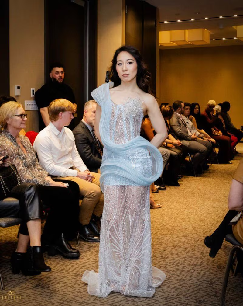 Model in an icy blue beaded gown with a sculpted fabric swirl walking a runway.